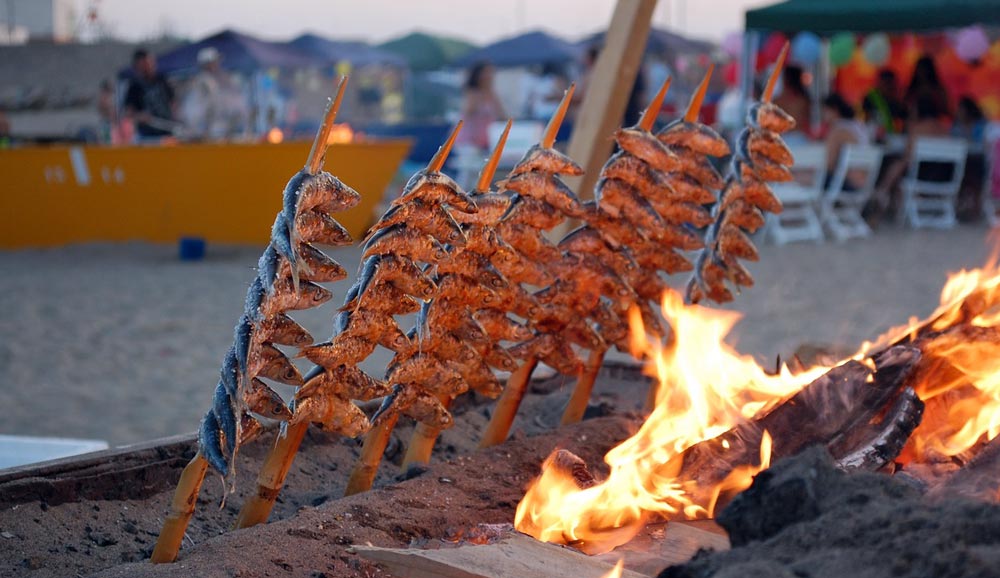 Typical atmosphere on the evening beach grilling freshly caught fish. Delicious local food is praised by Malaga property buyers.