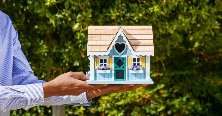 Real estate professional holding a doll house, symbolizing how easy it is to buy and sell houses with ibuyers